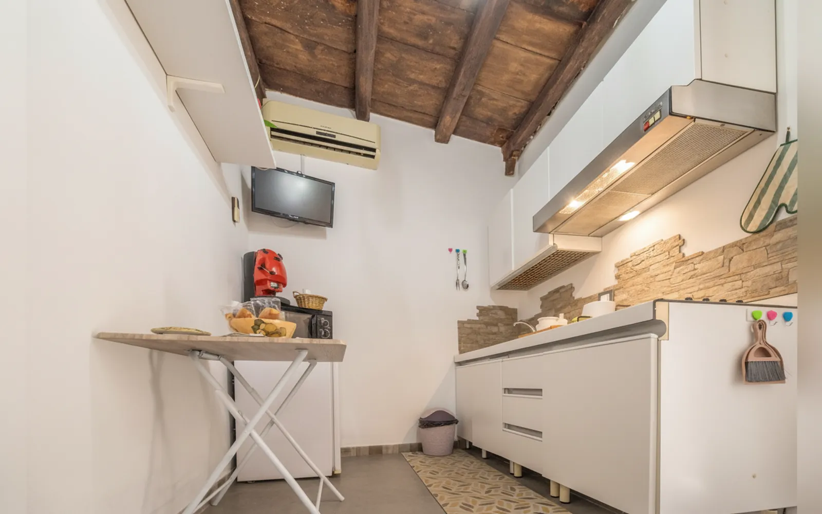La cucina con il tavolino, la TV a parete e il soffitto con le travi