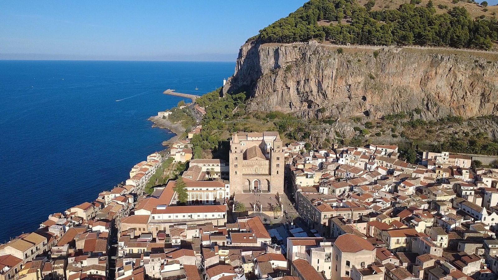 Veduta dall'alto di Cefalù: i tetti del centro storico, le torri del duomo, la Rocca a strapiombo e il mare blu