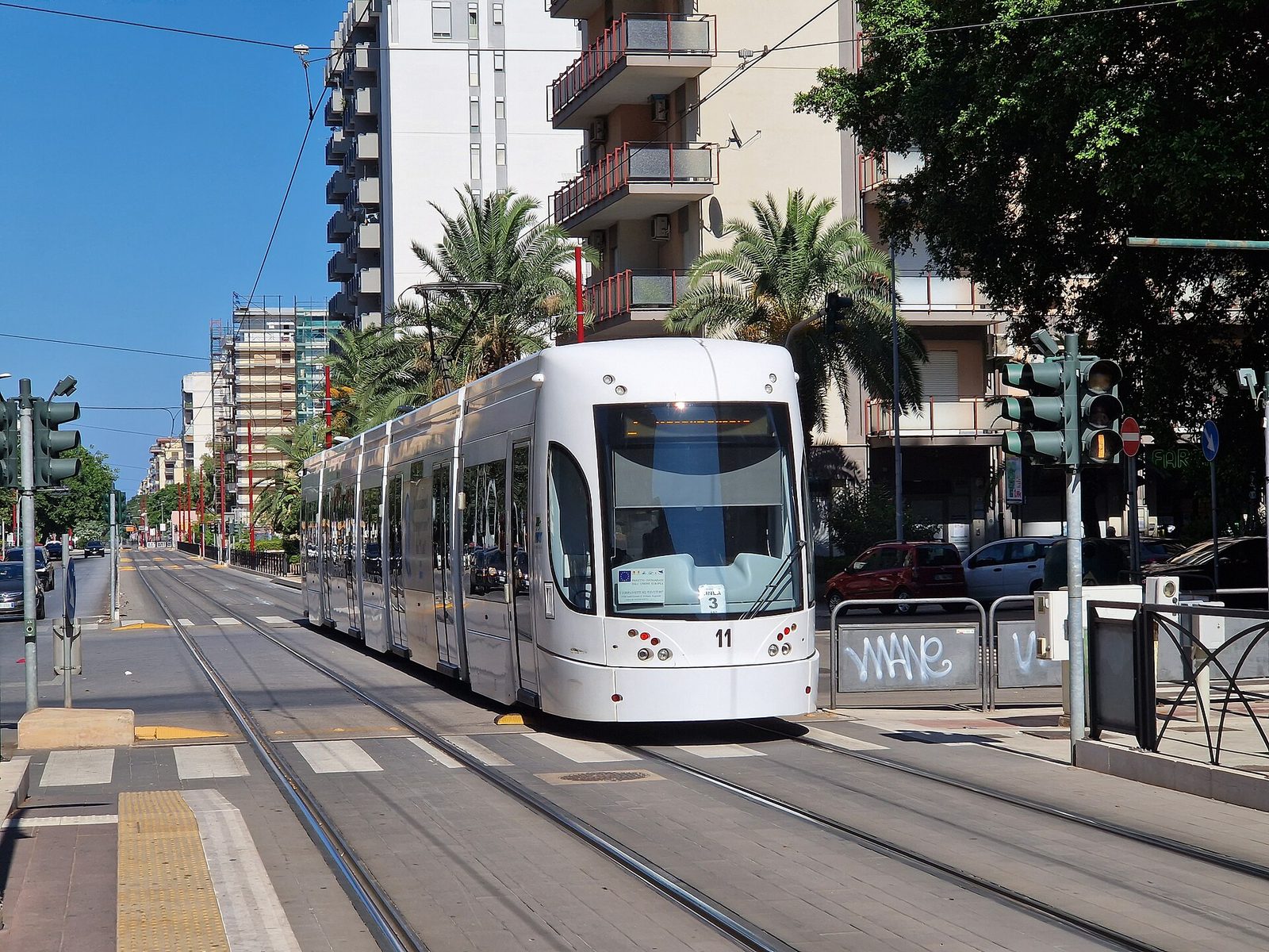 Un tram bianco della rete tranviaria di Palermo in servizio lungo un viale alberato con palme